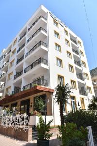 a large white building with a palm tree in front of it at Carpe Diem Apartments-Hotel in Shëngjin