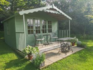 a green shed with a table and chairs in a yard at The Byre in Llandyfrydog