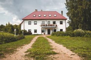 a large white house with a red roof and a dirt road at Šubrakkrasti in Vestiena