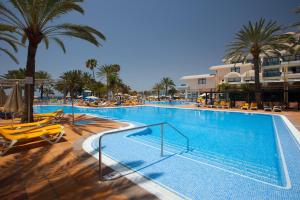 a large swimming pool with yellow chairs and palm trees at Grupotel Tres Vidas in San Agustin