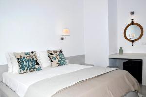 a white bedroom with a bed with pillows and a mirror at Petros Rooms in Koufonisia