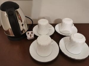 four cups and saucers on a table next to a coffee pot at Foresight Hostel in Tawau