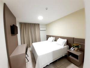 Habitación de hotel con cama blanca y TV en Agulhon Hotel en Primavera do Leste