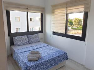 a bedroom with a bed with blue sheets and two windows at Kyrenia Comfort Apartments in Kérynia