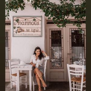 a woman sitting at a table in front of a building at Studio Cozy - In the Heart of Skyros Village in Skiros