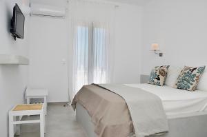 a white bedroom with a bed and a television at Petros Rooms in Koufonisia