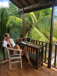 a woman sitting on a chair with a laptop on a table at Arjuna Uluwatu Guest House in Uluwatu