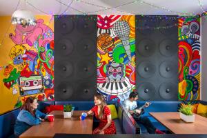 a group of people sitting at tables in a room with a mural at Let's Rock Party Hostel in Kraków