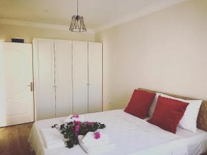ein weißes Bett mit roten Kissen und Blumen darauf in der Unterkunft Apart TU Çeşme in Izmir