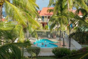 a resort pool with people in it with palm trees at Le Colibri - T2 les pieds dans l'eau in Saint-François