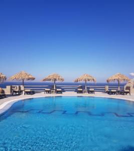 a swimming pool with chairs and umbrellas and the ocean at Hotel Gorgona in Mýkonos City