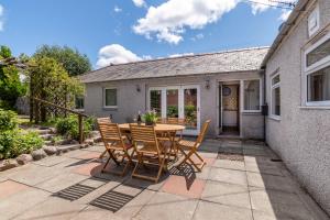 un patio con mesa y sillas frente a una casa en Dormie Cottage, lovely bright and spacious bungalow with wood fire, en Ballater