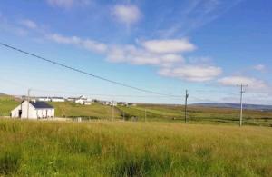 a field of grass with a white house in the distance at Cozy & Remote Hideaway Gintys Cottage in Ross Port