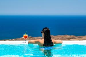 a woman sitting in a swimming pool with a drink at Siete Mares Luxury Suites in Imerovigli