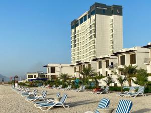 a row of lounge chairs on a beach with a tall building at Mirage Bab Al Bahr Beach Hotel in Dibba