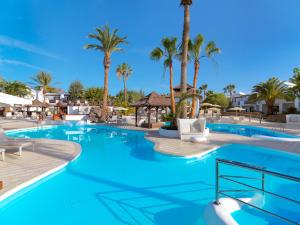 a swimming pool with palm trees and blue water at Boutique Hotel H10 White Suites - Adults Only in Playa Blanca