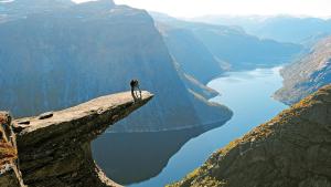 奧達的住宿－Trolltunga Odda Apartments，站在悬崖边缘俯瞰湖泊的人