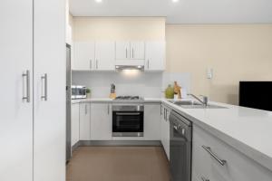 a white kitchen with a sink and a stove at The Banq Apartments by Urban Rest in Sydney