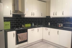uma cozinha com armários brancos e uma parede de azulejos pretos em F3 Cosy Single Room (Sandycroft Guest House) em Londres