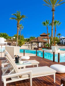 une terrasse avec des chaises et une piscine bordée de palmiers dans l'établissement Boutique Hotel H10 White Suites - Adults Only, à Playa Blanca