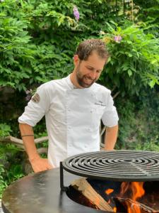 a man in a white shirt standing next to a grill at Casa della Capra in Mergozzo