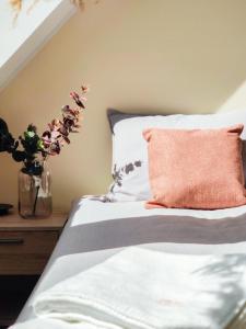 a bed with an orange pillow and a vase with flowers at Pensjonat Sztynort in Sztynort
