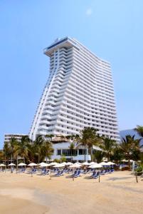 - un grand bâtiment sur une plage avec des chaises et des parasols dans l'établissement HS HOTSSON Hotel Acapulco, à Acapulco