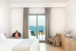 a hotel room with a bed, chair, table and window at Mykonos Soul Luxury Suites in Agios Stefanos