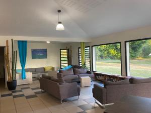 a living room with couches and chairs and windows at Auberge de Poé in Bourail