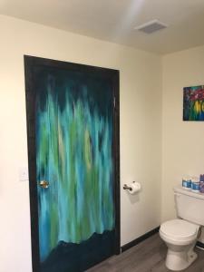 a bathroom with a toilet and a painting on the door at Fox n Fireweed Cabins in Tok