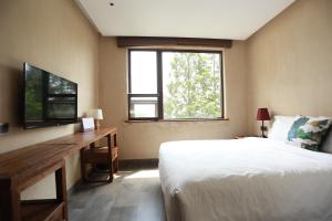 Schlafzimmer mit einem Bett, einem Schreibtisch und einem TV in der Unterkunft TOP ZERO HOTEL in Wudangshan