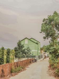 a green building on a dirt road next to a fence at Nhiên Homestay - The Green House in Phú Quốc
