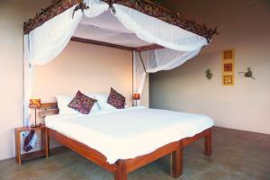 a bedroom with a canopy bed with white sheets and pillows at Kikonko Lodge in Buseruka