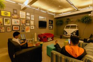 two men sitting in chairs in a room with a car on the wall at Joy Hostel & Suítes in Brasília
