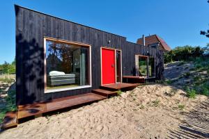 a black house with a red door on a pile of sand at Duinvis 15 in Oostduinkerke