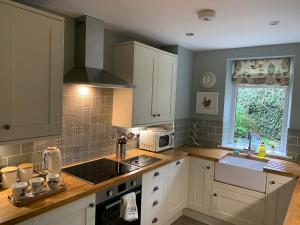 a kitchen with white cabinets and a sink and a window at Withens Way Holiday Cottage, 2 Bedrooms, Haworth in Haworth