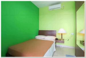a green room with a bed and a lamp at The Nancy's Homestay Pekanbaru Mitra RedDoorz in Pekanbaru