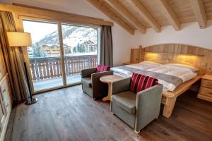 a bedroom with a bed and two chairs and a large window at Hotel City in Täsch