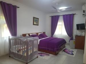 sypialnia z łóżkiem z fioletową pościelą i łóżeczkiem dziecięcym w obiekcie Charlestina Beach Resort w mieście Ampeni
