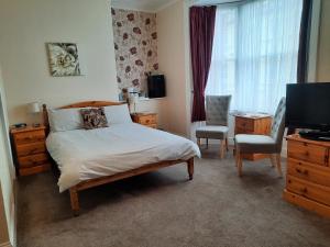 a bedroom with a bed and a television and chairs at Fosters Guest House in Weymouth