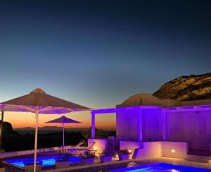 una piscina con iluminación púrpura y sombrilla en Katharos Pool Villas, en Oia