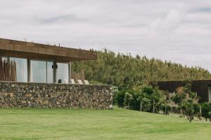 a house with a stone wall and a grass field at Santa Barbara Eco-Beach Resort in Ribeira Grande