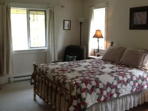 a bedroom with a bed and a chair and windows at Wisteria Honeymoon Cottage in Sooke