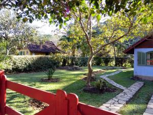 a red fence in front of a yard with a tree at Pousada Sítio das Astrapéias in Visconde De Maua