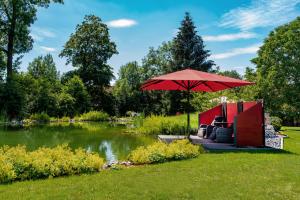 ein roter Regenschirm im Gras neben einem Teich in der Unterkunft Romantic Wooden Lodge,Sauna,Schwimmteich,alleinstehend,absolut ruhig in Hessisch Oldendorf + 18 Fotos