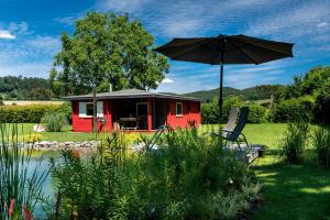 una casita roja con sombrilla y silla en Romantic Wooden Lodge,Sauna,Schwimmteich,alleinstehend,absolut ruhig, en Hessisch Oldendorf