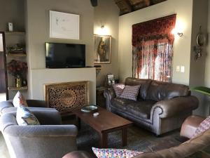 sala de estar con muebles de cuero y TV en 11 Raptors Lodge, en Hoedspruit