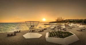 a beach with chairs and umbrellas and the ocean at Maistra Select Family Hotel Amarin in Rovinj