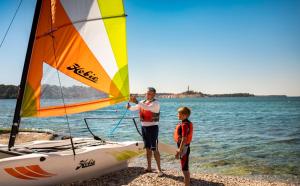 a man and a boy standing on the beach with a sailboat at Maistra Select Family Hotel Amarin in Rovinj