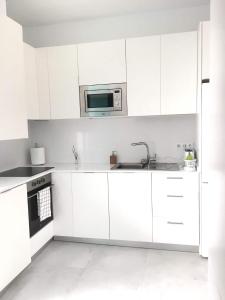 Biała kuchnia z białymi szafkami i kuchenką mikrofalową w obiekcie Casita cerca de la playa decorada con amor w mieście Tarifa